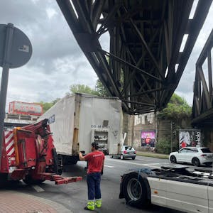 Ein Lkw steckt unter einer Brücke, ein Mitarbeiter eines Abschleppunternehmens steht davor.