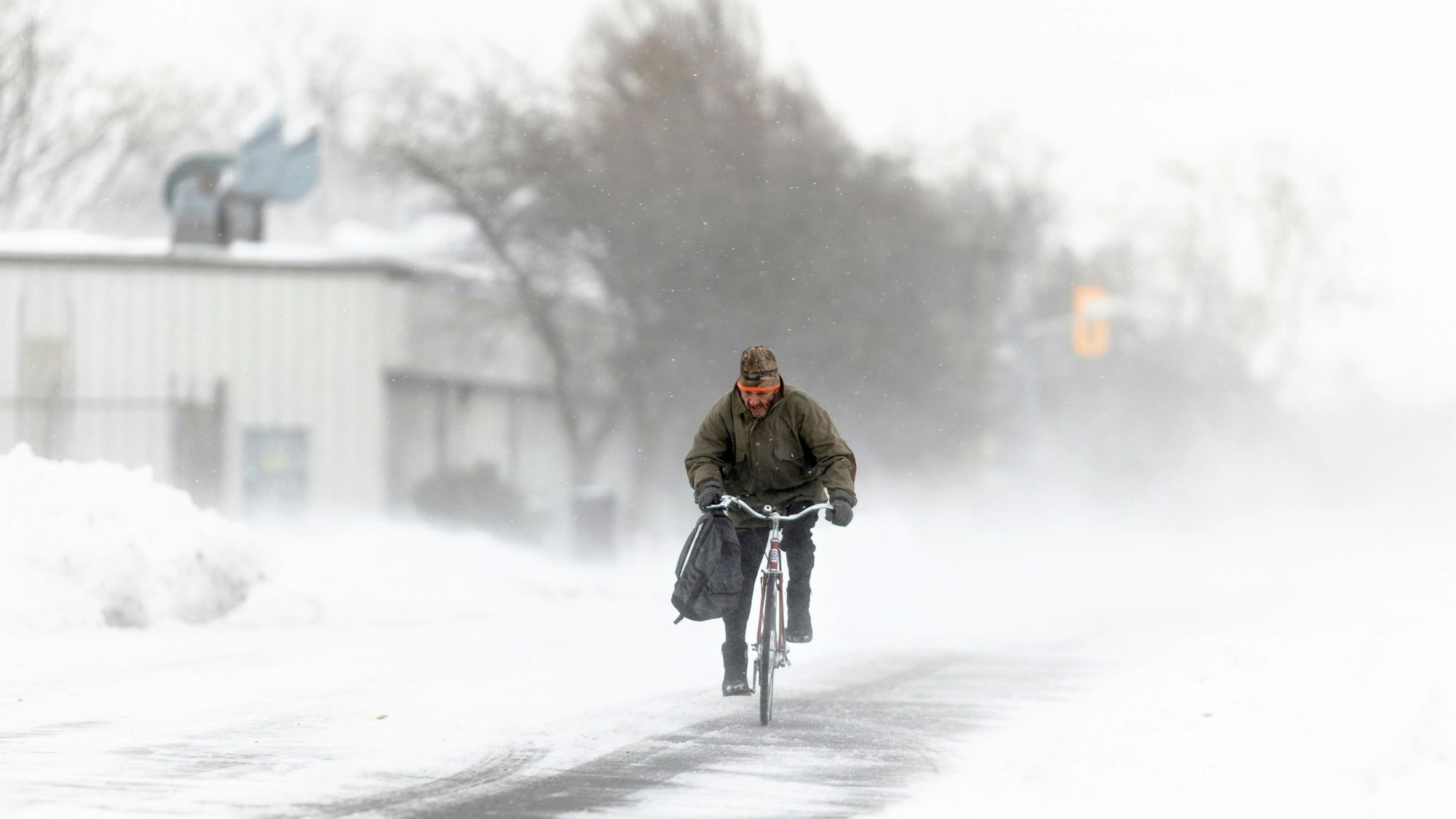 Ein Mann fährt mit seinem Fahrrad während eines Wintersturms auf einer schneebedeckten Straße.