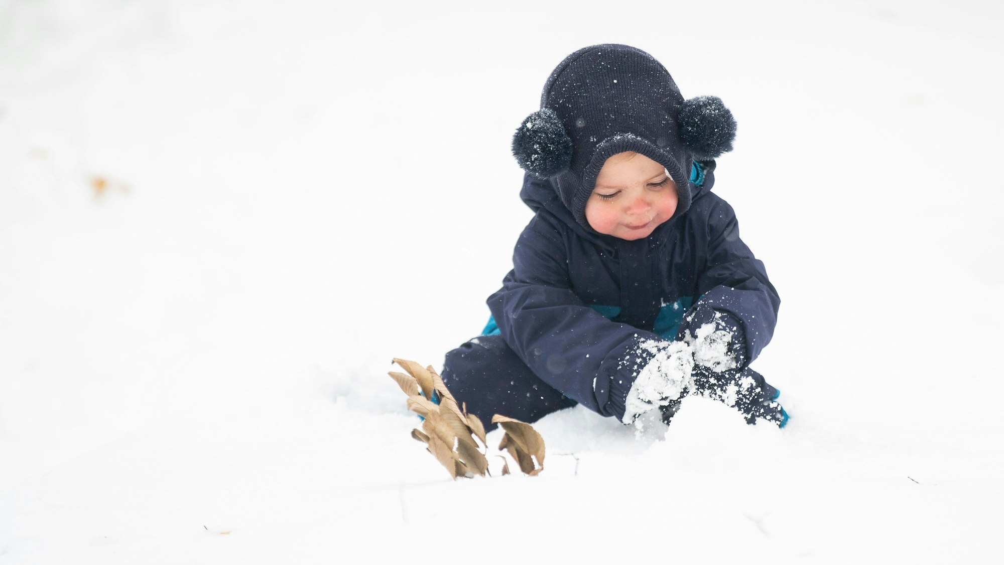Ein Kind strägt eine Mütze und spielt im Schnee.