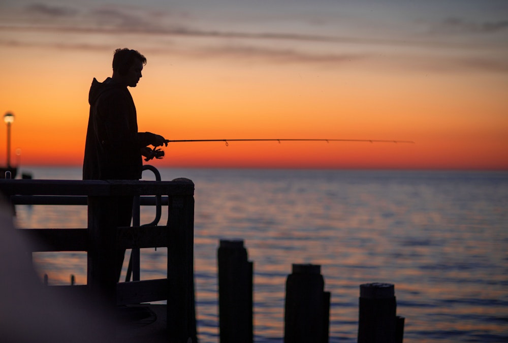 Ein Angler steht auf einer Seebrücke und wartet darauf, dass ein Fisch anbeißt (Symbolbild)