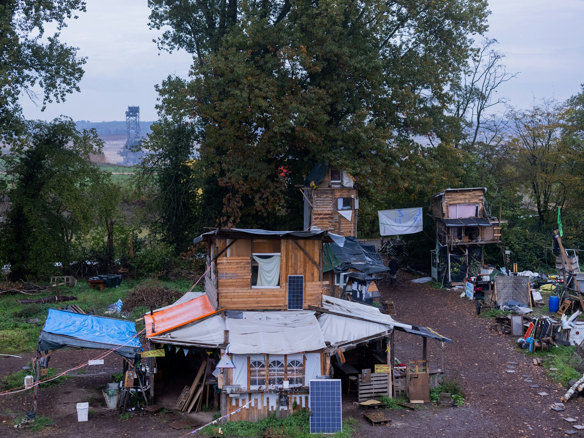 Holzhäuser stehen im Protestcamp von Umweltaktivisten - im Hintergrund arbeitet ein Braunkohlebagger.