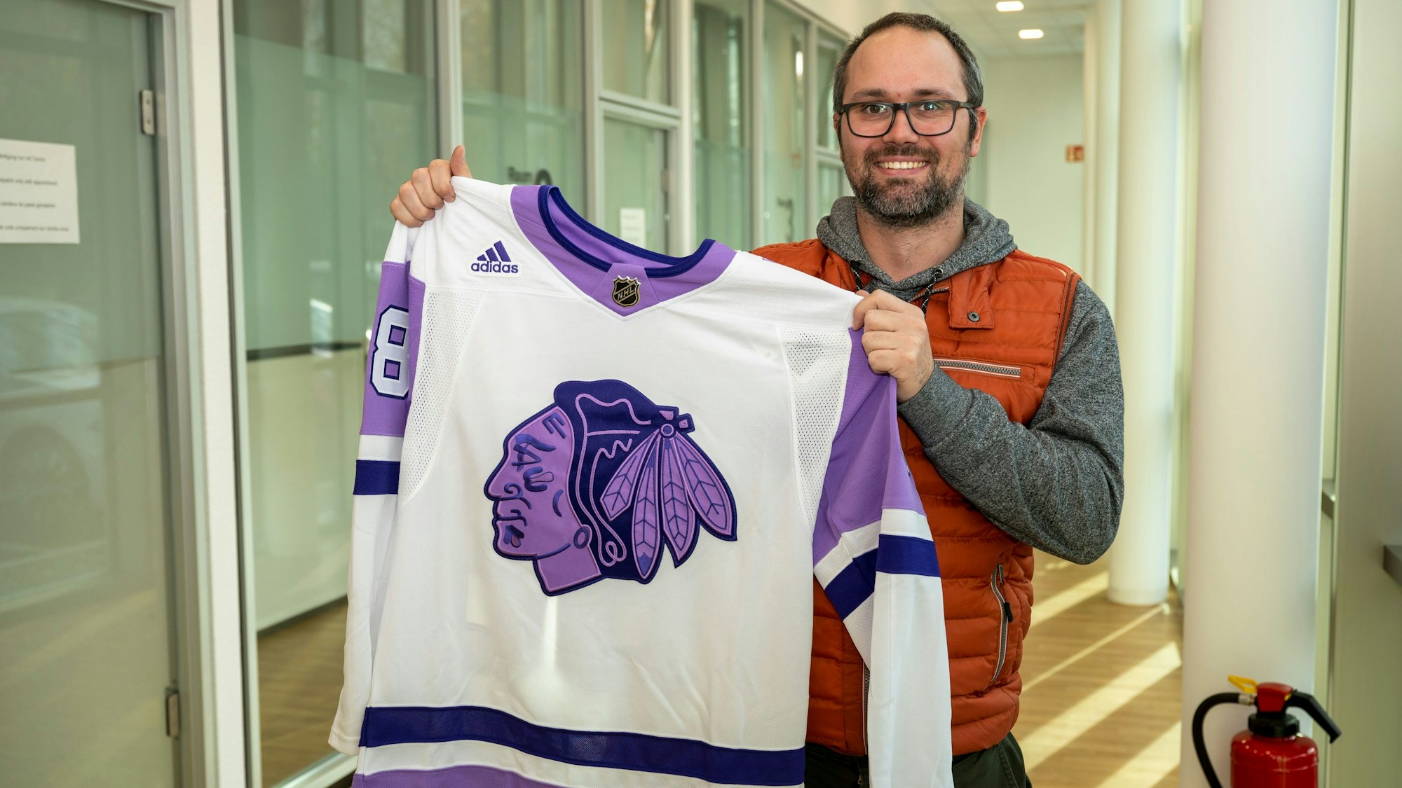 Marc Böhm hält ein Eishockey-Trikot der Chicago Blackhawks hoch, das sein Onkel ihm aus den USA geschickt hat.