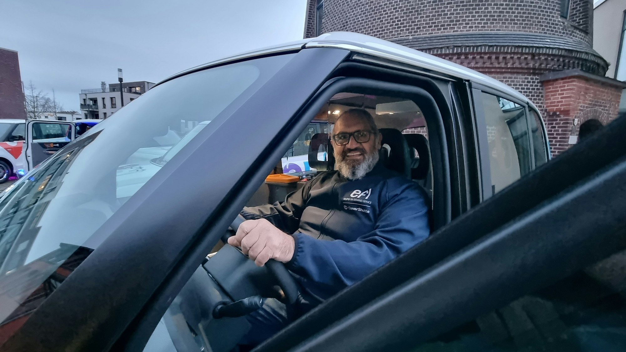 Pascuale Martino, ein bärtiger Mann mit Brille sitzt am Steuer und schaut durch die geöffnete Fahrertür in die Kamera. Er lächelt.