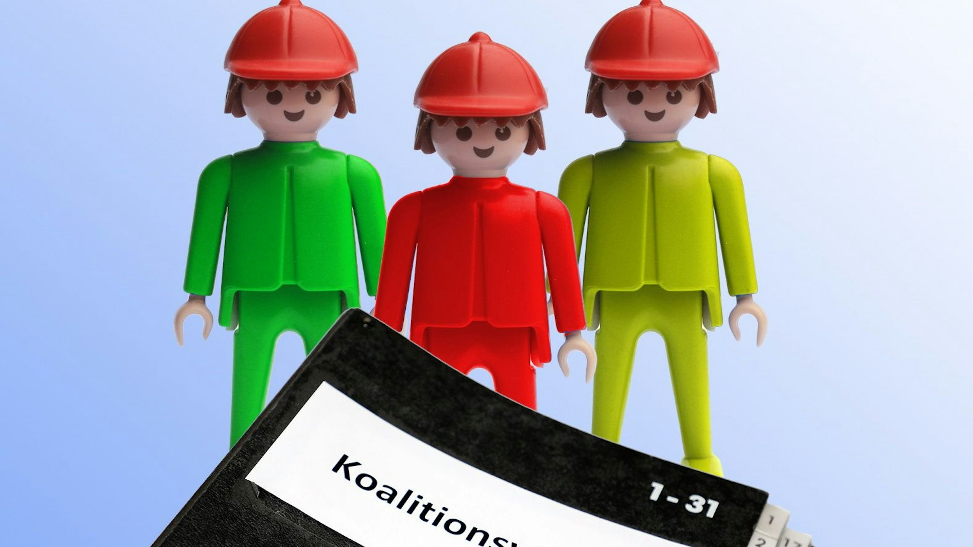 Ein grüner, ein roter und ein gelber Playmobilmensch stehen hinter einer Mappe mit der Aufschrift „Koalitionsvertrag“.