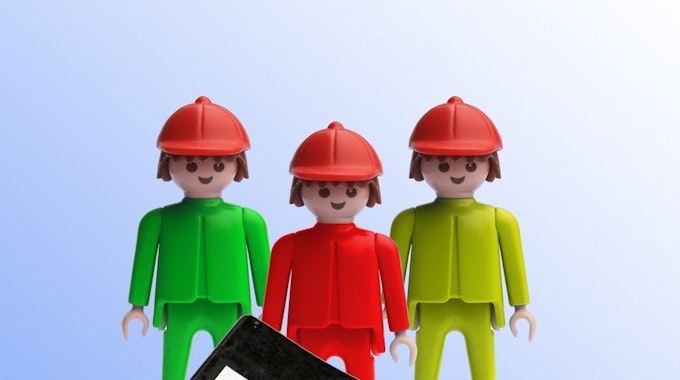 Ein grüner, ein roter und ein gelber Playmobilmensch stehen hinter einer Mappe mit der Aufschrift „Koalitionsvertrag“.