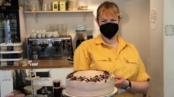 Eine Frau im gelben Hemd präsentiert eine vegane Torte.