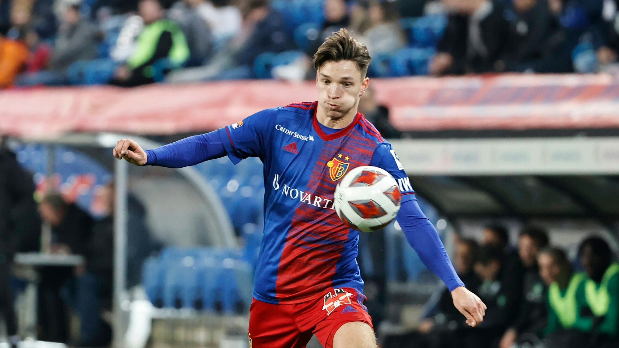 Noah Katterbach trägt das blau-rote Trikot des FC Basel und nimmt den Ball an der Seitenlinie an.