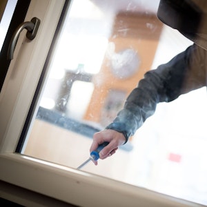 Ein Einbrecher macht sich mit einem Schraubenzieher an einem Fenster zu schaffen.