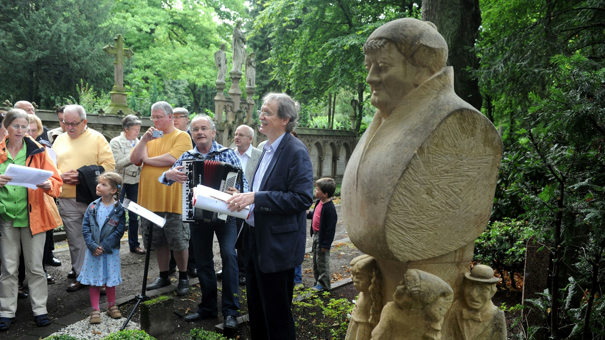 An der Gedenkstätte für Johann Christoph Winters, den Gründer des Hänneschen-Theaters, auf dem Melatenfriedhof haben sich mehrere Menschen versammelt. Zu sehen ist auch unser Autor Wolfgang Oelsner, der eine Rede hält.