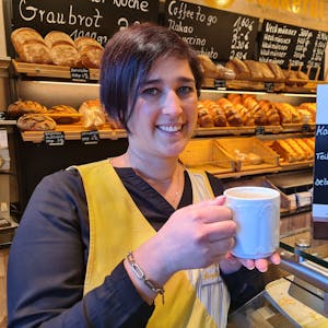 Jessica Küpper hält einen Kaffee in der Hand und steht vor dem Brotregal der Bäckerei Küpper in Bedburg.