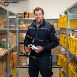 Zoll-Sprecher Jens Ahland steht zwischen Regalen mit Paketen, die der Zoll aus dem Verkehr gefischt hat, und hält eine Drohne in der Hand, die in Deutschland nicht zugelassen ist.