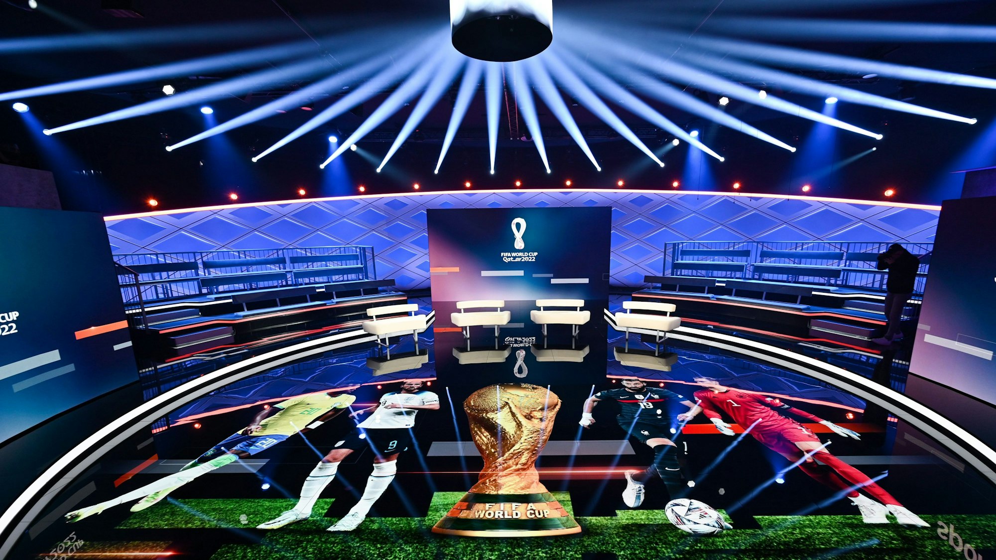 Das WM-Studio von Ard und ZDF ist in einem Halbkreis aufgebaut. Auf dem Boden werden verschiedene WM-Stars um den WM-Pokal her projiziert. Das Studio ist durch die Beleuchtung in ein dunkles Blau getönt.