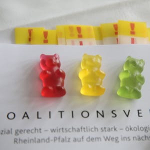 ILLUSTRATION - Ein rotes, ein gelbes und ein grünes Gummibärchen liegen auf dem Exemplar eines Koalitionsvertrages.