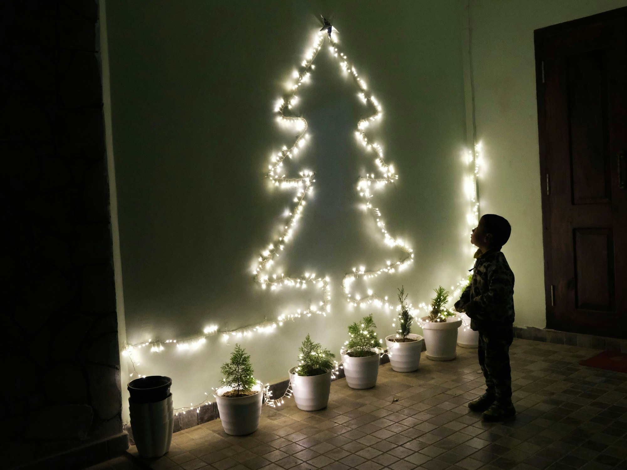 Ein Kind betrachtet an einer Wand eine Lichterkette in Form eines Weihnachtsbaumes.