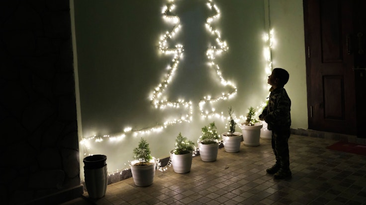 Ein Kind betrachtet an einer Wand eine Lichterkette in Form eines Weihnachtsbaumes.