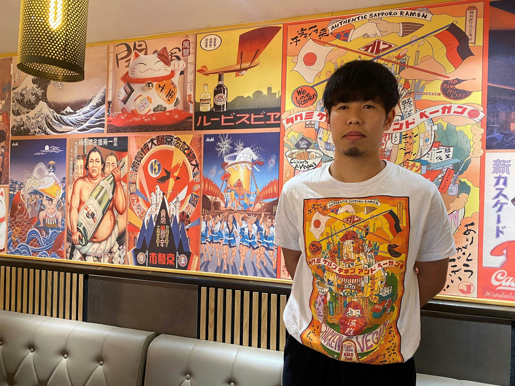 Der Japaner Keita Kinoshita steht vor einer Wand mit typischen japanischen Kunstwerken.