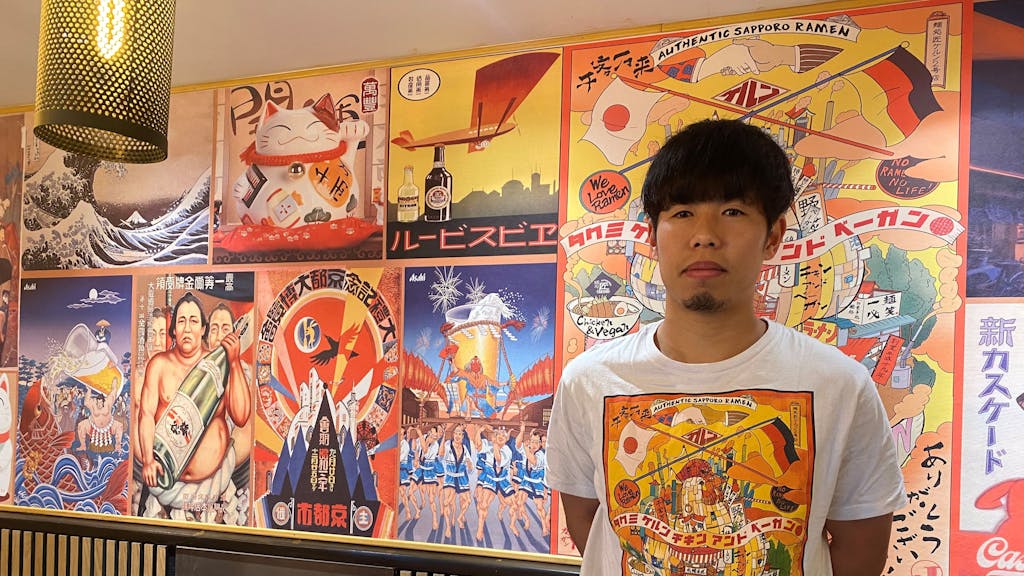 Der Japaner Keita Kinoshita steht vor einer Wand mit typischen japanischen Kunstwerken.