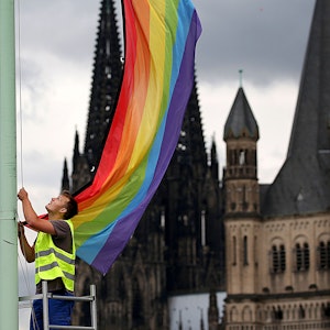 Ein Arbeiter hängt in Köln vor der Kulisse des Doms und der Kirche Groß St. Martin eine Regenbogenfahne auf.