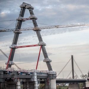 Die zwei neuen Pylone der Leverkusener Brücke sind im Vordergrund zu sehen. Es ist eine große Baustelle. Im Hintergrund ragt der alte Pylon in den leicht bedeckten Himmel.