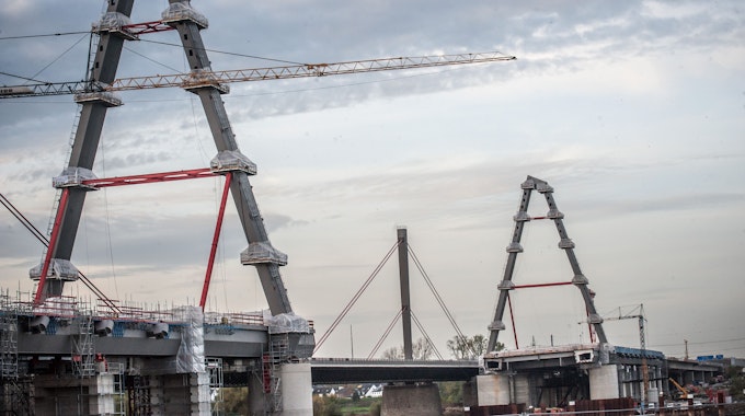 Die zwei neuen Pylone der Leverkusener Brücke sind im Vordergrund zu sehen. Es ist eine große Baustelle. Im Hintergrund ragt der alte Pylon in den leicht bedeckten Himmel.