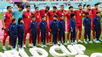 Die iranische Nationalmannschaft steht vor dem Anpfiff auf dem Rasen und schweigt bei der Nationalhymne ihres Landes.