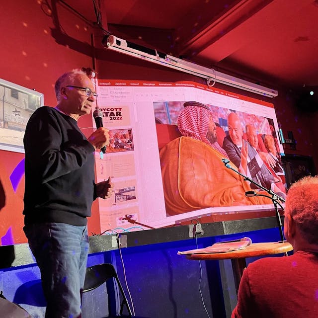 Dietrich Schulze-Marmeling hält einen Vortrag vor Publikum, im Hintergrund sieht man eine Power-Point-Präsentation