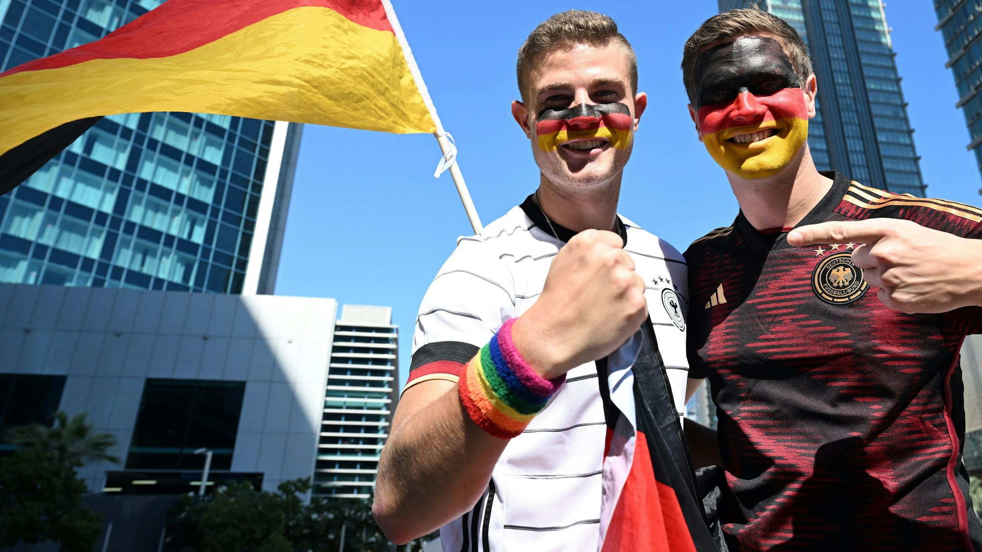 Bengt (l.) und Jan Kunkel stehen bei der Mobilen Fan-Botschaft des DFB in Doha. Bengt Kunkel zeigt das Regenbogen-Schweißband an seiner rechten Hand. Beide tragen Deutschland-Trikots.