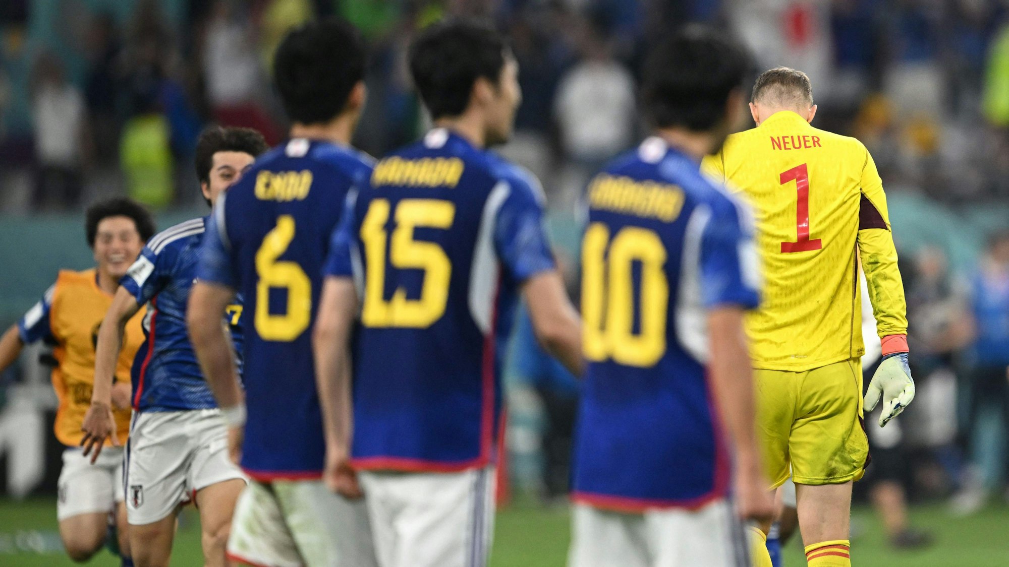 Manuel Neuer verlässt mit gesenktem Haupt das Spielfeld, während um ihn herum die japanische Nationalmannschaft jubelt.