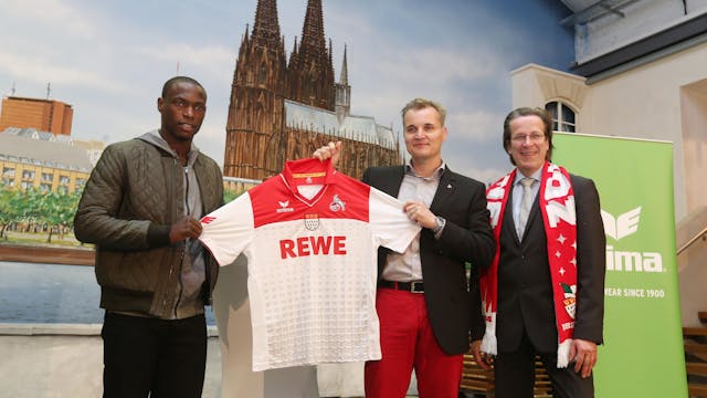 Frank Sahler, Leiter Marketing/Vertrieb beim 1. FC Köln, präsentiert ein früheres Trikot des Bundesligisten. Er hält ein rot-weißes Trikot des 1. FC Köln in der Hand.