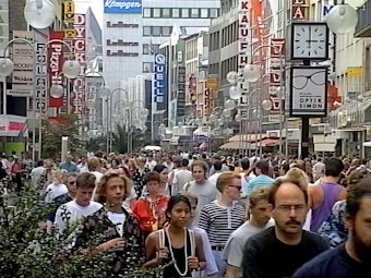 Das Bild zeigt eine Einkaufsstraße in Köln mit zahlreichen Menschen.