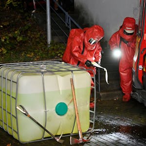 Feuerwehrleute in Chemikalienschutzanzügen untersuchen einen Kunststofftank.