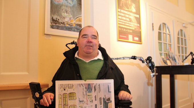Ein Mann im Rollstuhl hat ein Bild mit einer Straßenansicht auf dem Schoß.