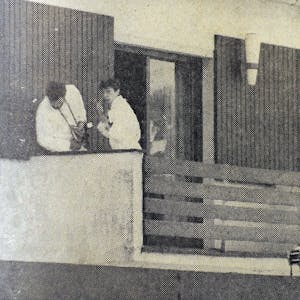 Zwei Beamte in weißen Anzügen suchen auf einer Veranda Spuren