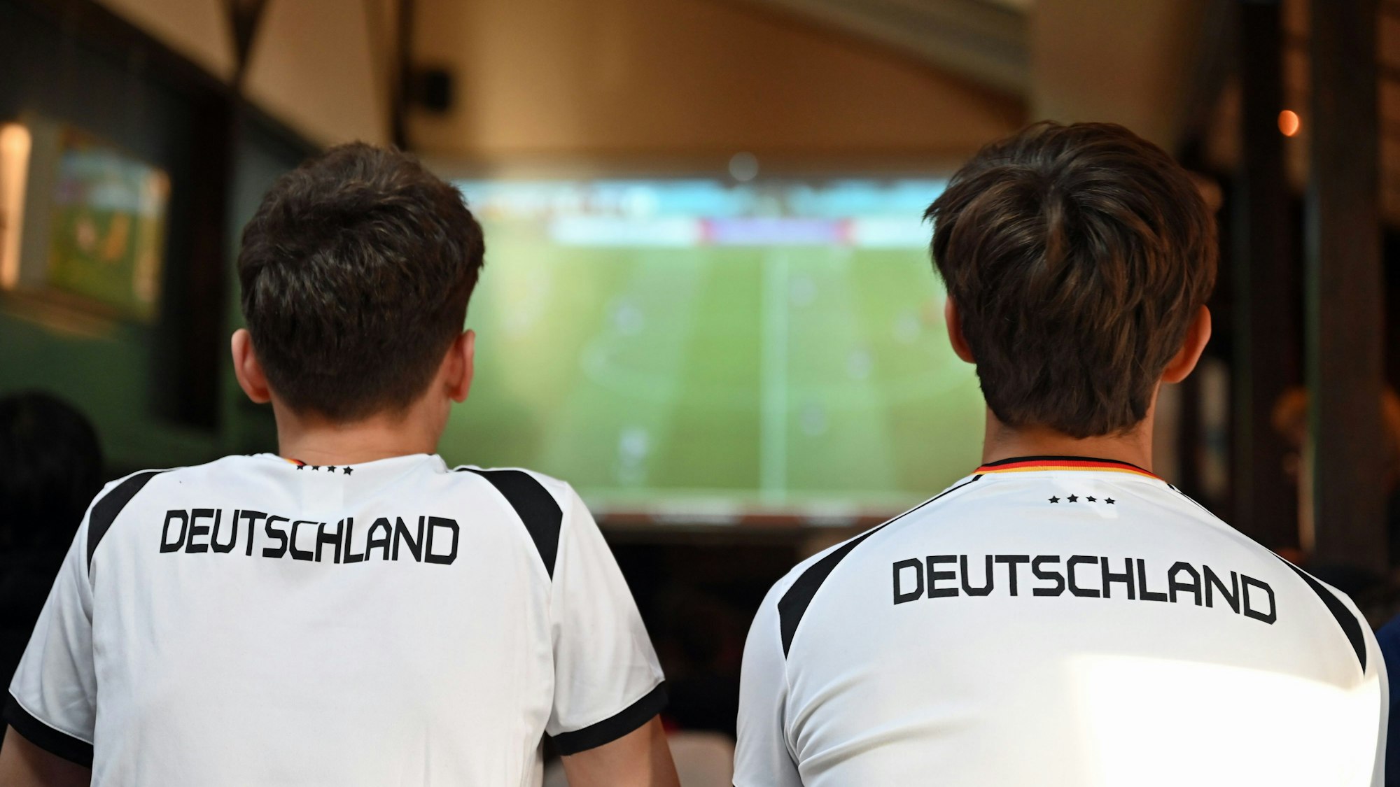 Zwei junge Männer schauen im Deutschland-Trikot Fußball im TV.