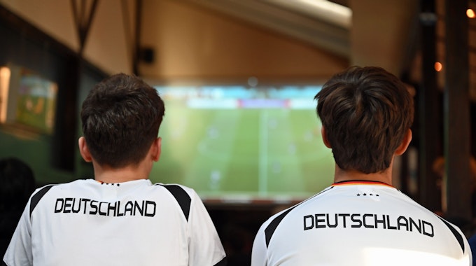 Zwei junge Männer schauen im Deutschland-Trikot Fußball im TV.