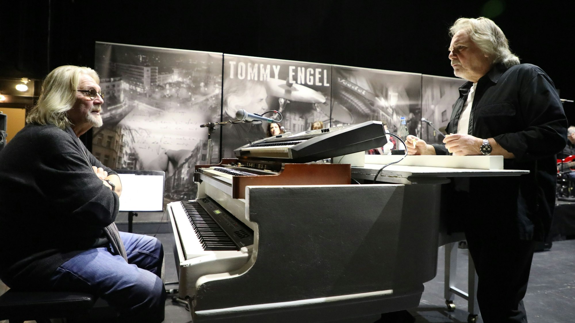 Jürgen Fritz sitzt am Piano, Tommy Engels steht am Flügel und spricht mit ihm.