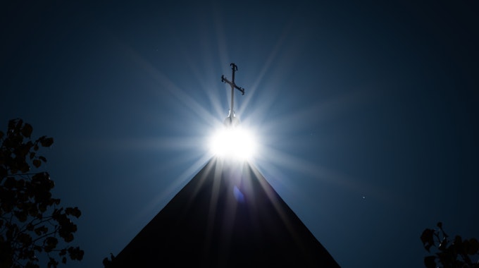 Die Sonne strahlt unter einem Kreuz auf dem Dom Osnabrück.
