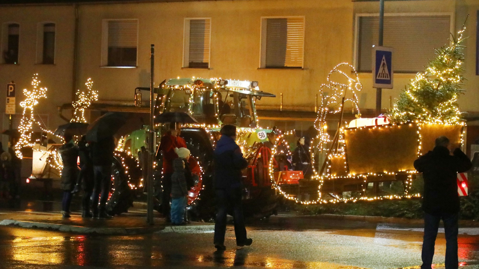 Ein leuchtender Weihnachtsmannschlitten wird von einem Traktor über die Straße gezogen.