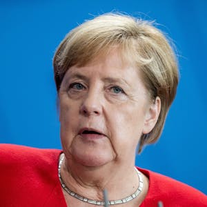 Ex-Bundeskanzlerin Angela Merkel blickt bei einer Pressekonferenz ins Publikum. Die CDU-Politikerin steht vor einer blauen Wand.