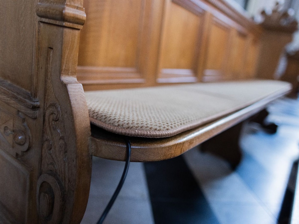 Ein beheiztes Sitzkissen (ein Prototyp) liegt auf einer Bank in der St. Mariä Himmelfahrt Kirche.