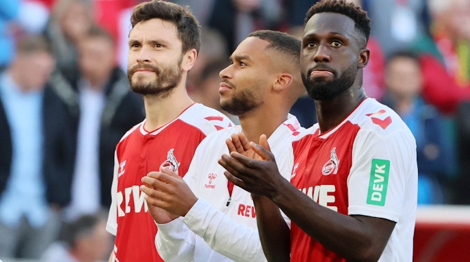 Kingsley Schindler stet mit Linton Maina und Jonas Hector nach dem Bundesliga-Heimspiel des 1. FC Köln gegen Borussia Dortmund vor der Südkurve.