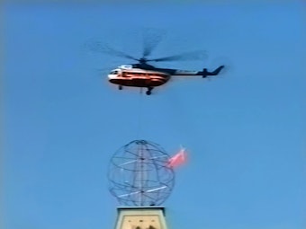 Das Bild zeigt einen Helikopter, der über der Weltkugel von HA Schult fliegt.