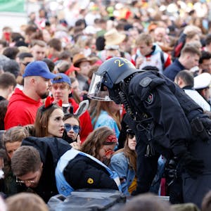 Ein Polizist kommuniziert mit einer jungen Frau im Teufel-Kostüm, im Hintergrund stauen sich Menschenmassen vor den Absperrungen zur Zülpicher Straße.