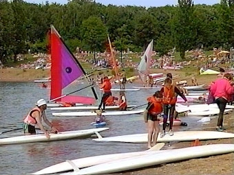 Das Bild zeigt mehrere Menschen an einem kleinen Strandabschnitt, die sich mit mehreren Boards und Segeln bereit fürs Windsurfing machen.