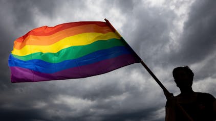 Eine Frau trägt die Regenbogenfahne bei einer Gedenkfeier. (Symbolbild)