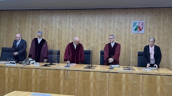 Die Richter und Beisitzer stehen im Gerichtssaal hinter ihren Pulten