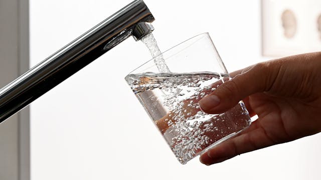 Eine Hand hält ein Wasserglas unter einen Wasserhahn.