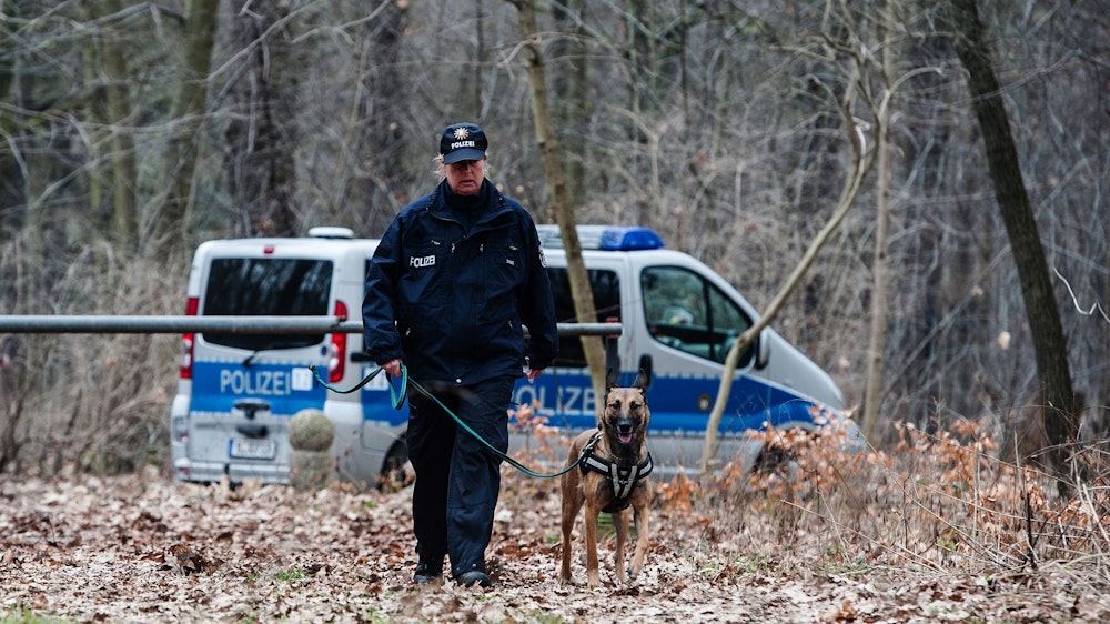 Eine Hundeführerin der Polizei geht mit ihrem Hund durch den Wald.