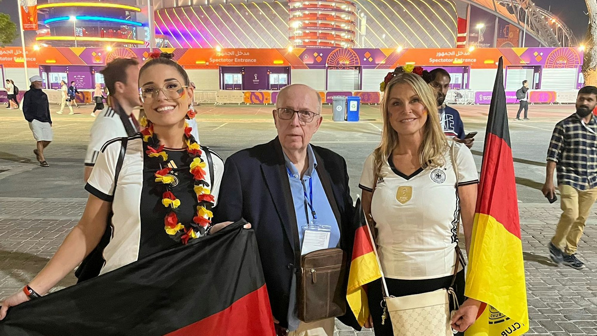 Reiner Calmund, der ein dunkelblaues Sakko trägt, lässt sich nach dem WM-Spiel zwischen Deutschland und Japan mit den deutschen Fans Elena (l.) und Elke Stegili vor demKhalifa International Stadions in Al-Rayyan fotografieren.