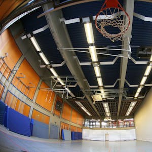 Eine leere Sporthalle im Schulzentrum Oberpleis. Oben ist ein Basketballkorb zu sehen, an einer Seitenwand lehnen blaue Sportmatten.